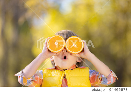 Surprised child holding slices of orange in autumn park 94466673