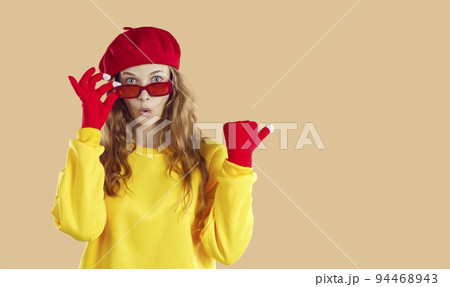 Surprised woman in yellow sweatshirt, red hat, gloves glasses looking at camera on beige background. Surprised woman in yellow sweatshirt, red hat, gloves glasses looking at camera on beige background. 94468943