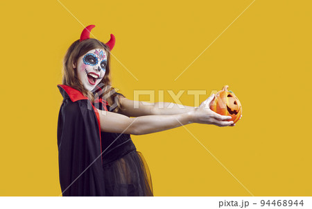Cheerful creative teenage girl in devil costume on Halloween having fun on orange background. Cheerful creative teenage girl in devil costume on Halloween having fun on orange background. 94468944