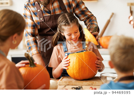 Happy girl helping dad carve Halloween pumpkin. Happy girl helping dad carve Halloween pumpkin. 94469395