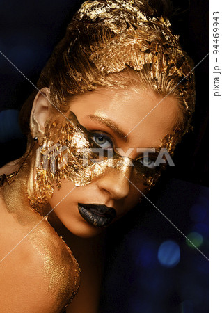 Fashion art Golden skin. Model girl with festive golden glamorous shiny professional make-up. Gold jewelry, bijouterie, accessories. Beautiful golden metallic body, black lips and skin. 94469943