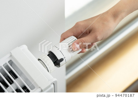 The woman turns off the heating by setting the radiator thermostat to a minimum 94470187
