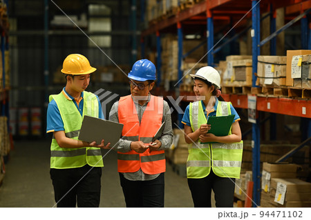 Middle aged manager and young workers inspecting stock and cardboard stock product on laptop computer in a large warehouse Middle aged manager and young workers inspecting stock and cardboard stock product on laptop computer in a large warehouse 94471102
