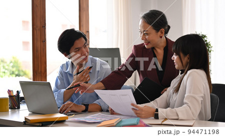 Smiling middle age female manager discussing new projects with young employees in bright office Smiling middle age female manager discussing new projects with young employees in bright office 94471198