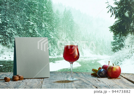 Glass of warm delicious mulled wine with fruits on wooden table on forest lake background 94473882