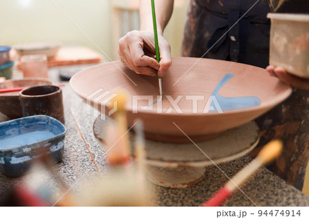 Potter woman paints a ceramic plate. Girl draws with a brush on earthenware. Process of creating clay products.. 94474914