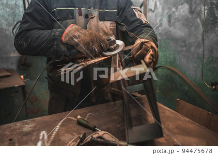 Worker does weld stripping with a grinder. Man works with iron in a workshop. Steel product manufacturing. 94475678