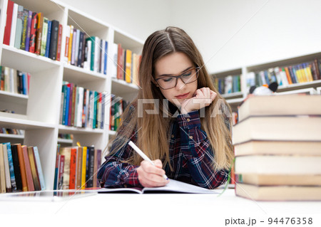 Girls writes in the library. Young student studying at the campus library.. 94476358