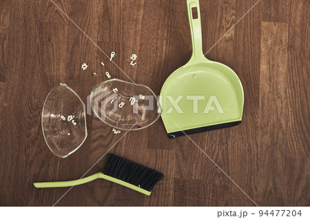 A close-up view from above of a split transparent cup with soup and brushes with a dustpan for cleaning. The concept of home cleaning in the apartment. High quality photo 94477204