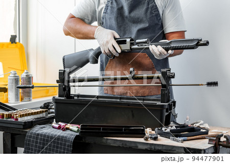 Close up of young man in apron disassembling a gun above the table 94477901