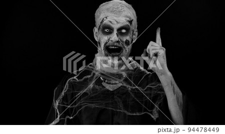 Inspired Halloween crazy zombie man pointing finger up with open mouth, showing Eureka gesture Inspired Halloween crazy zombie man pointing finger up with open mouth, showing Eureka gesture 94478449