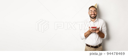 Holidays and celebration. Happy man having birthday party, making wish on b-day cake and smiling, standing against white background 94478469