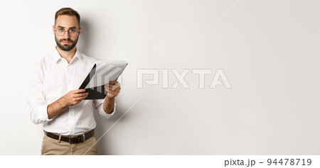 Serious employer looking at camera while reading documents on clipboard, having job interview, standing over white background Serious employer looking at camera while reading documents on clipboard, having job interview, standing over white background 94478719