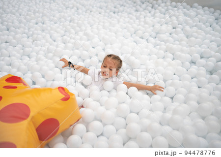 Happy little girl playing white plastic balls pool in amusement park. playground for kids. Happy little girl playing white plastic balls pool in amusement park. playground for kids. 94478776
