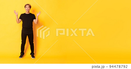 Full-length of surpirsed and excited, smiling blond asian guy raising hands up amazed, yellow background Full-length of surpirsed and excited, smiling blond asian guy raising hands up amazed, yellow background 94478792