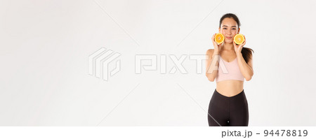 Sport, wellbeing and active lifestyle concept. Silly and cute asian fitness girl, female athlete losing weight with workout, gym trainings and healthy diet, showing two halves of orange Sport, wellbeing and active lifestyle concept. Silly and cute asian fitness girl, female athlete losing weight with workout, gym trainings and healthy diet, showing two halves of orange 94478819
