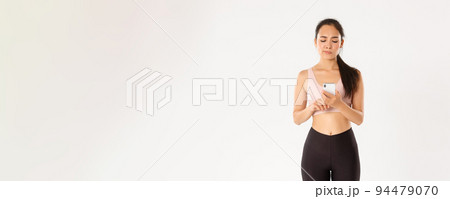 Sport, technology and active lifestyle concept. Fitness girl looking at her smartphone screen with upset face and smirk, disappointed with running results of workout tracker application Sport, technology and active lifestyle concept. Fitness girl looking at her smartphone screen with upset face and smirk, disappointed with running results of workout tracker application 94479070