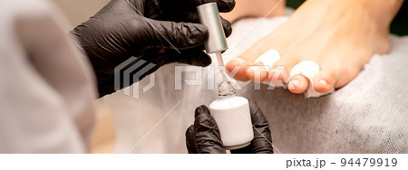White nail polish in the hands of a manicurist while painting nails on a female feet, closeup 94479919
