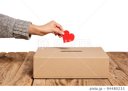 Charity. Red heart as symbol of peace, love is putting by female hand into slot of donation carton box. Concept of donorship, life saving or charity 94480231