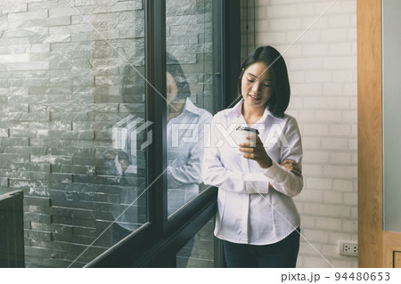 Happiness businesswoman holding takeaway coffee cup while standing at the window in the office. Happiness businesswoman holding takeaway coffee cup while standing at the window in the office. 94480653