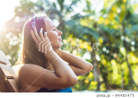 Happy smartphone woman relaxing near swimming pool listening with earbuds to streaming music. Beautiful girl using her mobile phone app 4g data to play songs while relaxing on summer luxury vacations Happy smartphone woman relaxing near swimming pool listening with earbuds to streaming music. Beautiful girl using her mobile phone app 4g data to play songs while relaxing on summer luxury vacations 94485475