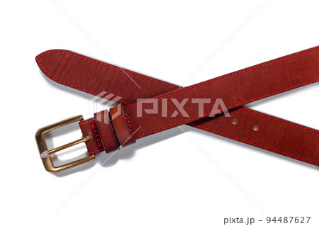 A crossed brown leather belt with a metal buckle on a white background is isolated. A crossed brown leather belt with a metal buckle on a white background is isolated. 94487627