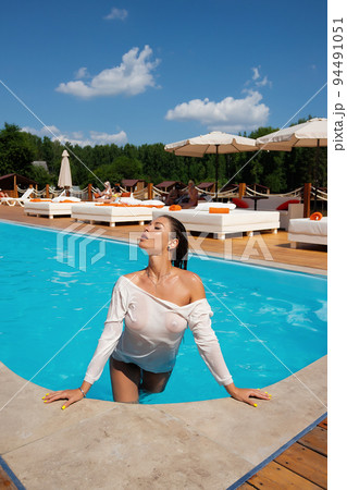 Sensual lady in wet dress standing in pool on sunny summer day Sensual lady in wet dress standing in pool on sunny summer day 94491051