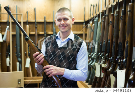 Smiling man standing in gun shop with hunting shotgun Smiling man standing in gun shop with hunting shotgun 94491133