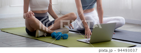 Young woman practicing exercise or yoga on mat while watching laptop computer tutorial online. 94493037