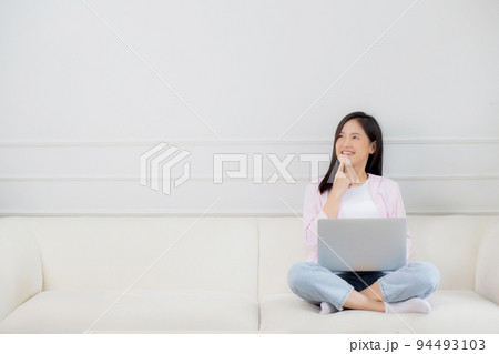 Young asian woman working on laptop computer sitting on sofa in the living room at home. 94493103