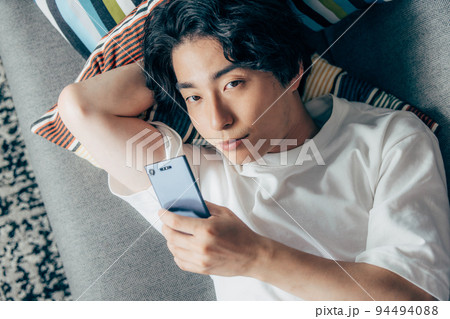 スマホを見ながら寝ている若い男性 94494088