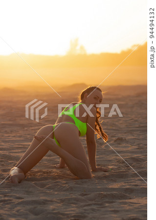 Seductive model in swimsuit kneeling on sandy beach Seductive model in swimsuit kneeling on sandy beach 94494132