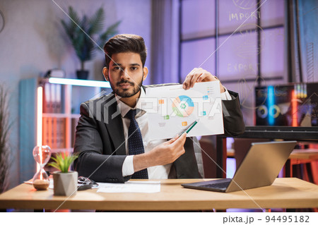 Confident arab financial expert office worker in suit working on laptop, showing paper report 94495182