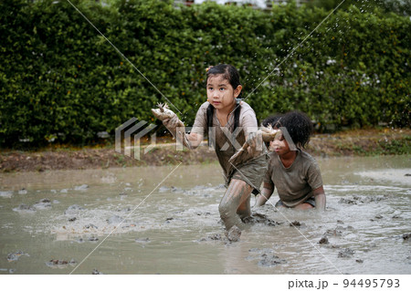 Two happy children child girl catching big frog in the large wet mud puddle on summer day. 94495793