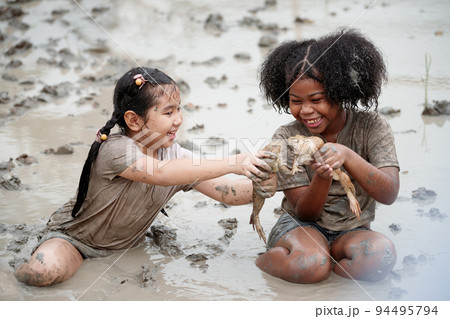 Two happy children child girl catching big frog in the large wet mud puddle on summer day. 94495794