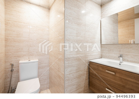 Simple bathroom with white toilet, wooden furniture and beige tiles. Modern interior of refurbushed apartment. 94496393