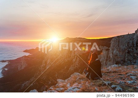 Selective focus. Beautiful tourist woman sitting on a rock high in the mountains, above the clouds and enjoying the sunset Copy space. The concept of calmness, silence and unity with nature 94496590