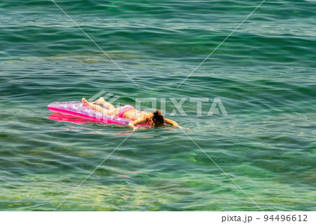 Summer vacation girl relaxing in sea on pink inflatable swimming pool air mattress bed floating in turquoise water background. Suntan at tropical beach. Summer vacation girl relaxing in sea on pink inflatable swimming pool air mattress bed floating in turquoise water background. Suntan at tropical beach. 94496612