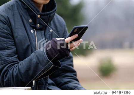 冬の屋外で指なし手袋でスマホを操作する男性 94497890