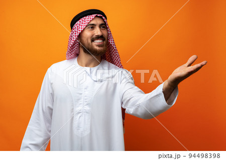 Young Arab man pointing hand to copy space on orange background Young Arab man pointing hand to copy space on orange background 94498398