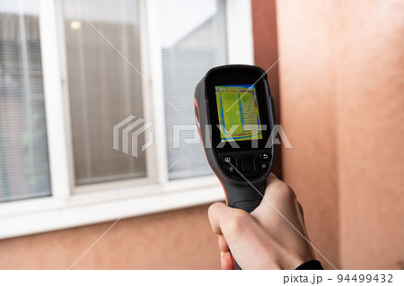 A male hand holds a thermal imager at the window of a house. Search for heat loss in private houses A male hand holds a thermal imager at the window of a house. Search for heat loss in private houses 94499432