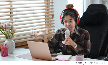 Young podcaster using a microphone and laptop computer recording audio for channel in home studio 94500057