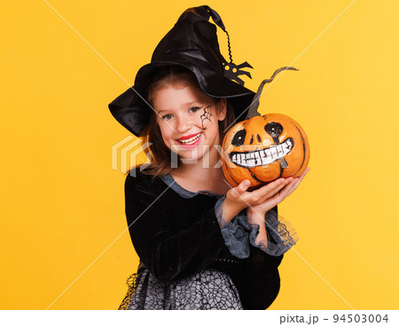 Happy girl in witch costume with pumpkin jack-o-lantern celebrates Halloween and laughs on yellow background Happy girl in witch costume with pumpkin jack-o-lantern celebrates Halloween and laughs on yellow background 94503004