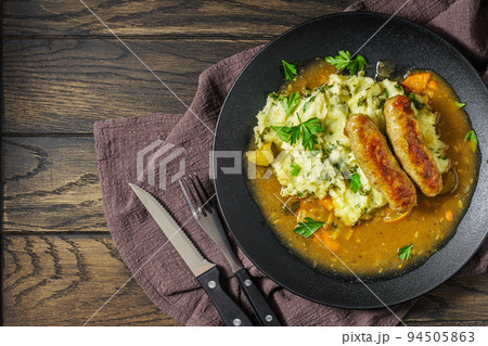 Dutch stamppot of potatoes, kale and sausages with gravy on plate above 94505863