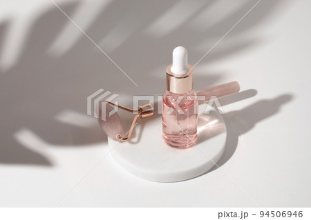 Massage quartz roller and pink glass bottle of cosmetic liquid transparent gel on white background. Dropper bottle, hyaluronic acid, oil, serum. Facial massage and relaxation. Gua Sha massage tools. Massage quartz roller and pink glass bottle of cosmetic liquid transparent gel on white background. Dropper bottle, hyaluronic acid, oil, serum. Facial massage and relaxation. Gua Sha massage tools. 94506946