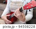 Young woman playing red ukulele at home, sitting on the floor, dressed as a hipster, learning songs 94508228