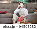 Cozy young hipster woman in casual wear drinks hot coffee from white cup, takes a break between learning to play ukulele guitar, sitting on floor in living room at home, leisure concept 94508232