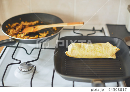 Cooking burrito, Mexican food at home. Grilled wheat tortilla stuffed with cheese, chicken, beans, corn, lettuce, tomato and sauce 94508817
