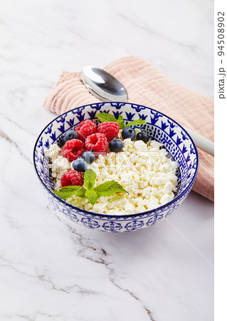 Cottage cheese in bowl decorated with raspberries and blueberries and mint leaves on white Cottage cheese in bowl decorated with raspberries and blueberries and mint leaves on white 94508902