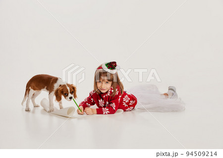 Portrait of beautiful little girl, child posing with dog isolated over white studio background. Writing letter to Santa 94509214
